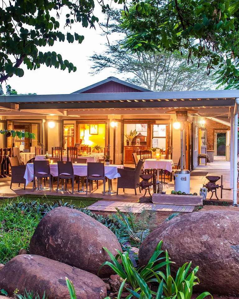 BIWEDA's main lodge and open veranda lit up at dusk, with garden boulders in the foreground