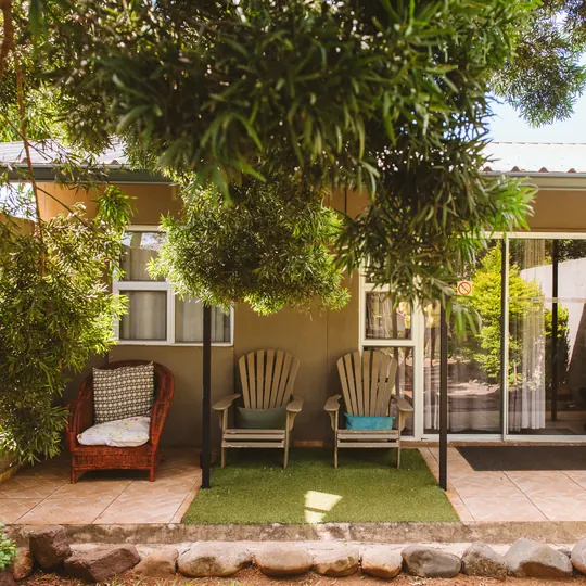 A shaded guest-room patio with garden chairs, opening onto BIWEDA's leafy grounds