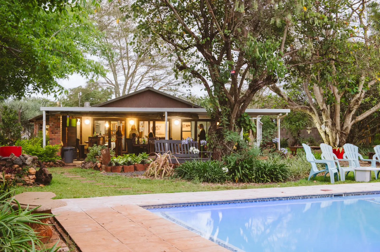 BIWEDA's lodge glowing in the late-afternoon light beside the pool and lawns, framed by tall indigenous trees